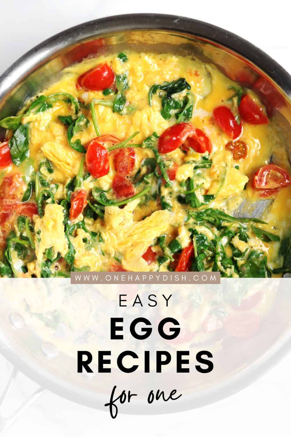 Scrambled eggs with wilted spinach and cherry tomatoes in a metal skillet, with text overlay: Easy Egg Recipes for One and the website www.onehappydish.com displayed across the middle.