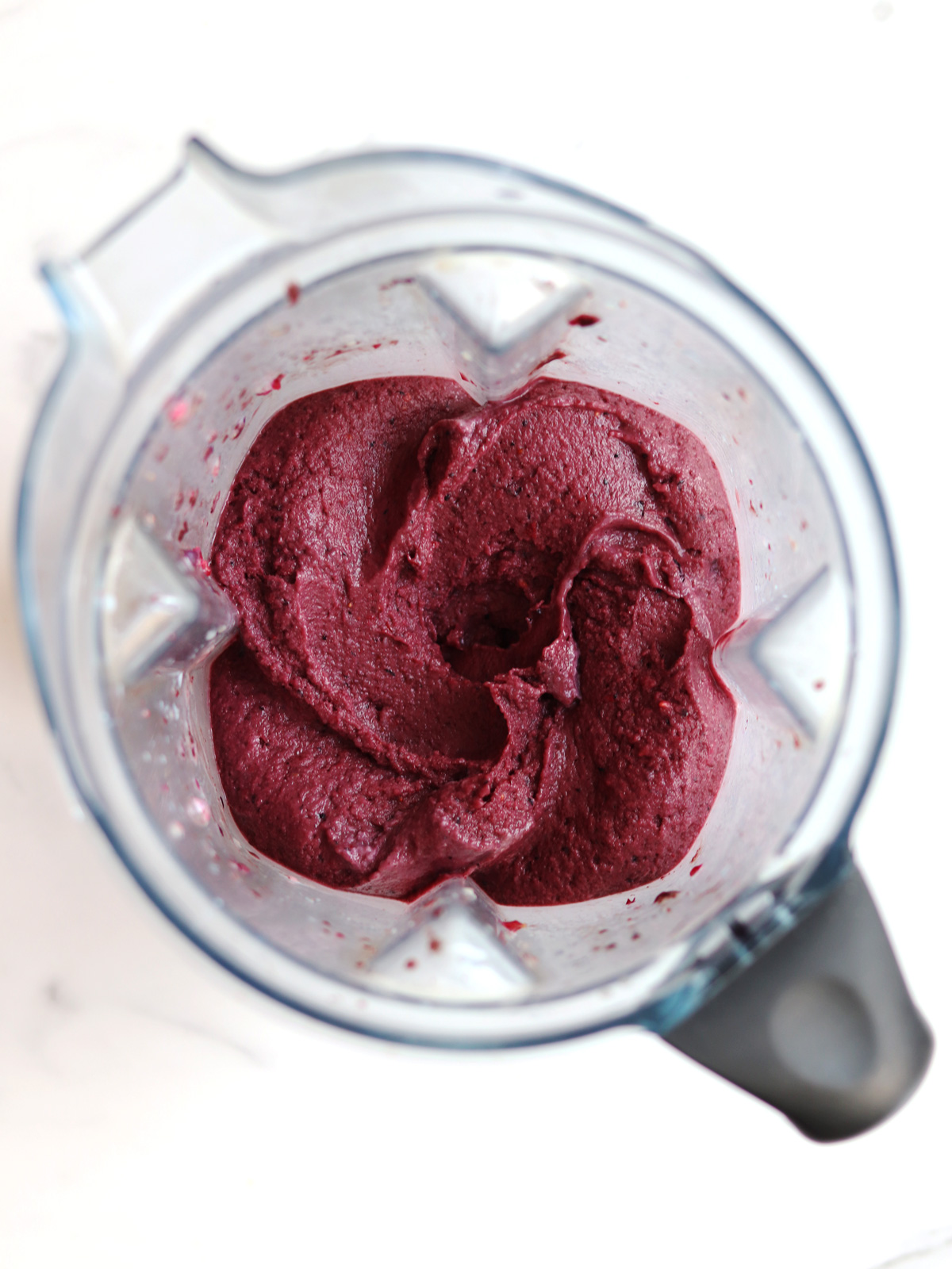 A blender filled with thick, smooth, acai blended mixture, viewed from above on a white countertop.