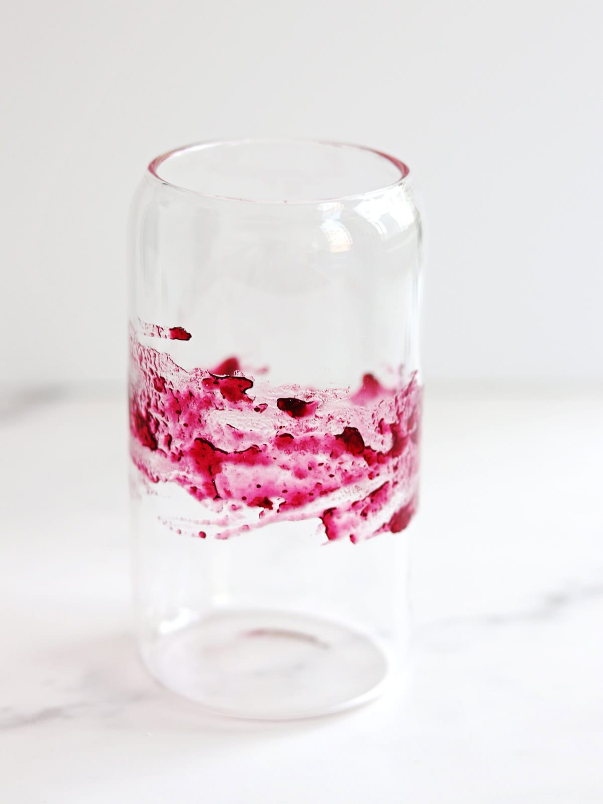 A clear smoothie glass with blueberry jam smeared around the middle sits on a white marble countertop.