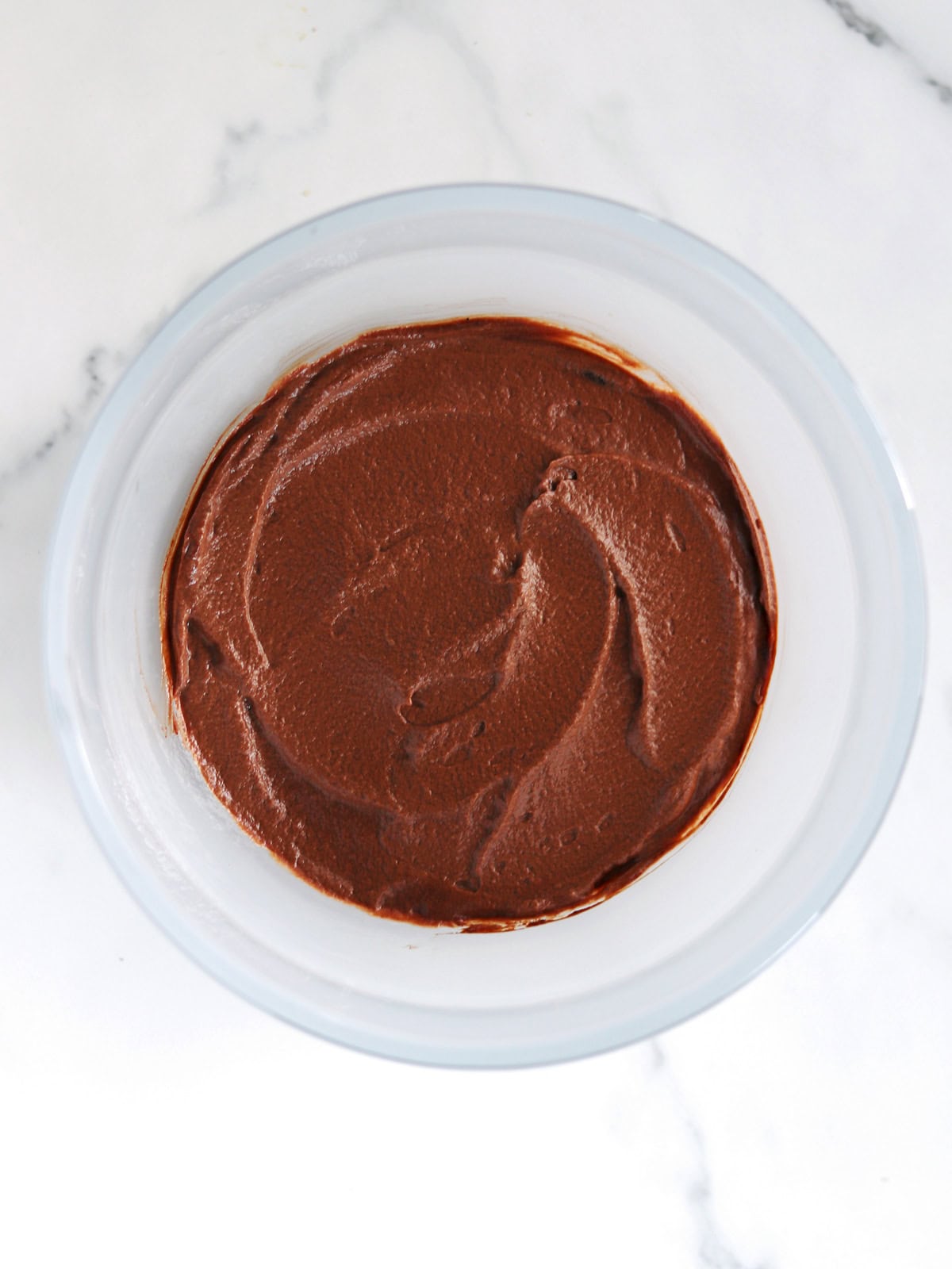 A frosted glass bowl containing freshly made chocolate mousse sits on a white marble countertop.