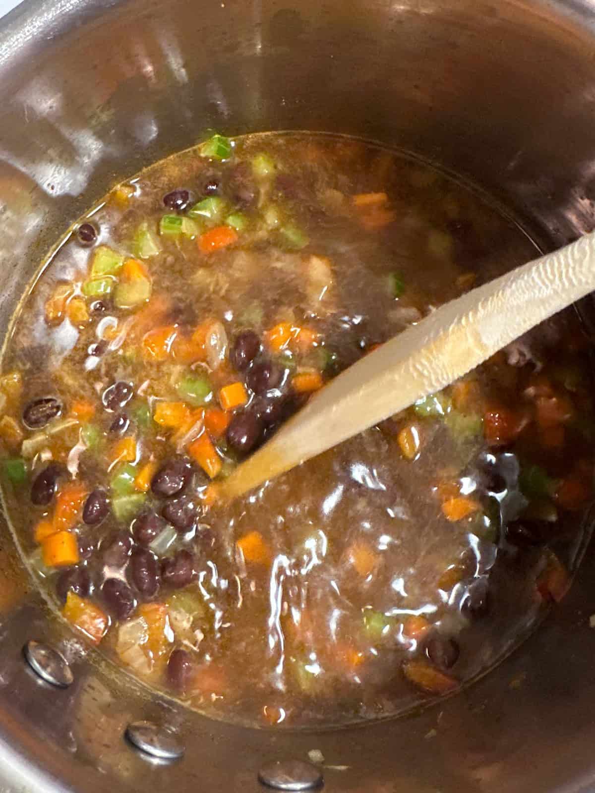 A pot of black bean soup being stirred with a wooden spoon.