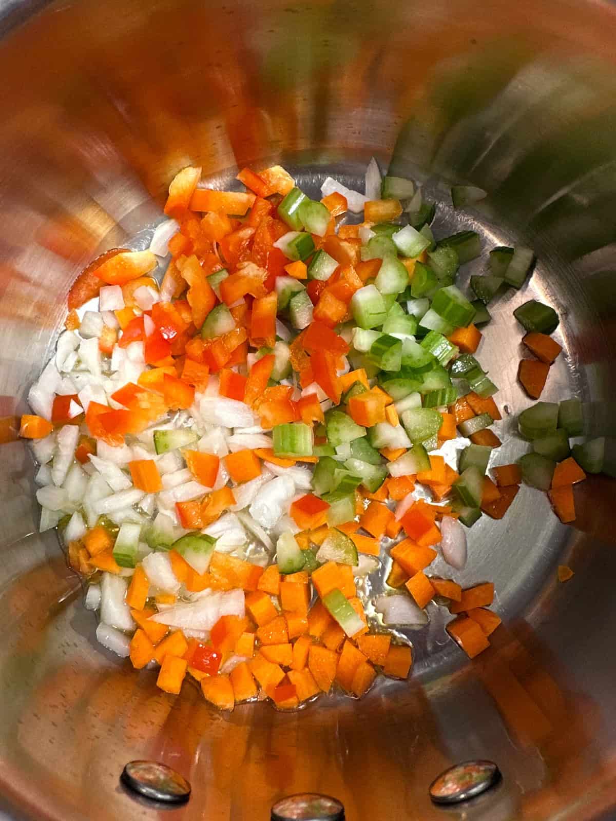 Diced onions, carrots, celery, and red bell pepper in the bottom of a stainless steel pot, cooking in olive oil.
